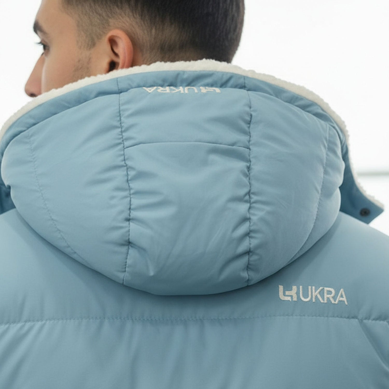 Close-up of UKRA embroidered logo on hood of blue puffer jacket.